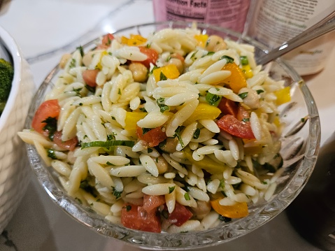 Close-up view of a fresh orzo salad bowl filled with lime juice and tomatoes peppers and herbs