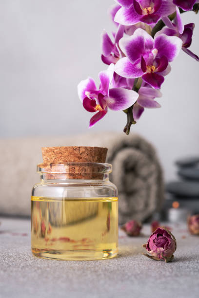 istock Spa still life featuring essential oils, smooth pebbles, a rolled grey towel, and a vibrant purple orchid 2148437636