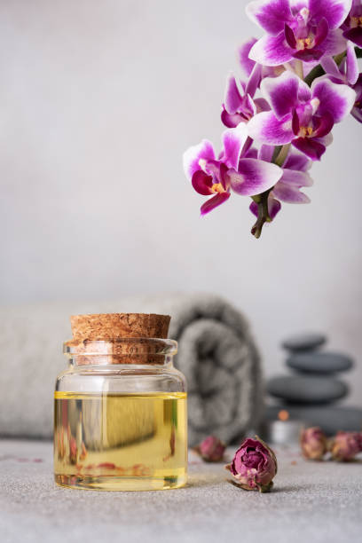 istock Spa still life featuring essential oils, smooth pebbles, a rolled grey towel, and a vibrant purple orchid 2148437695