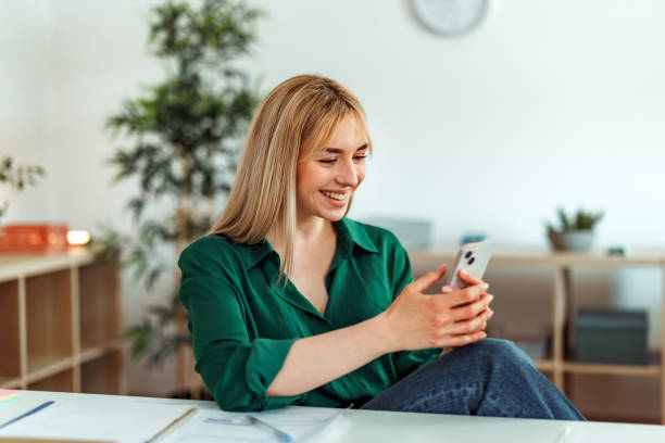 istock Smiling beautiful young woman text messaging on smart phone at home office 2148439604