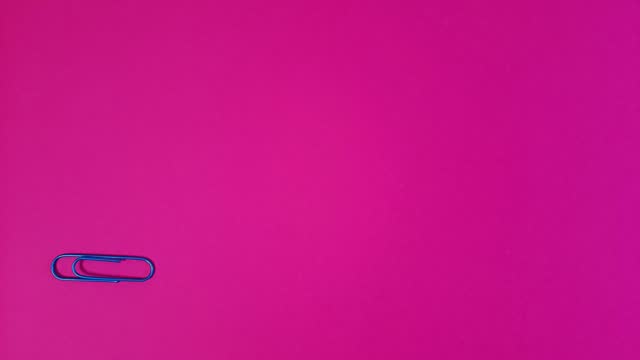 Blue paper clip rotates on pink background.