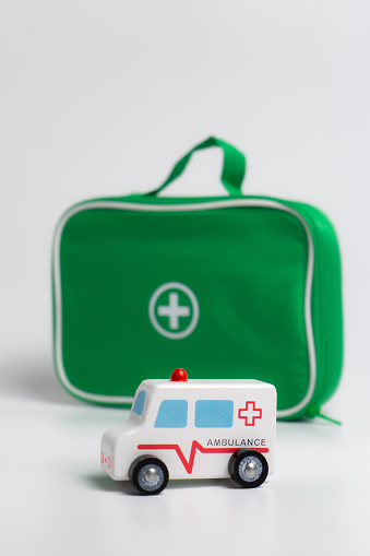 kids first aid kit, green bag with medical tools and wooden ambulance toy car isolated on white background