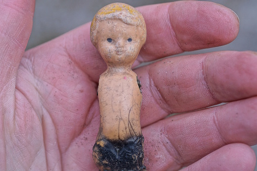 one small brown plastic charred broken doll toy lies on a hand