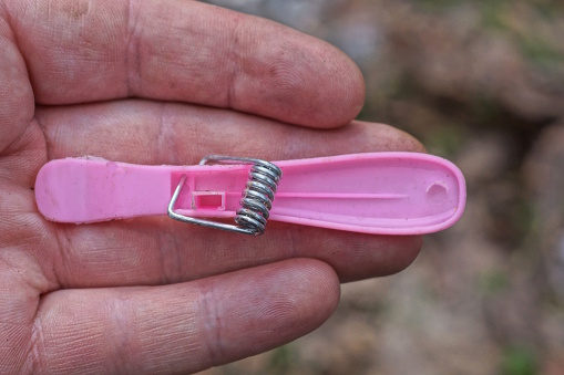 one piece of broken pink plastic clothespin lies on the fingers of the hand