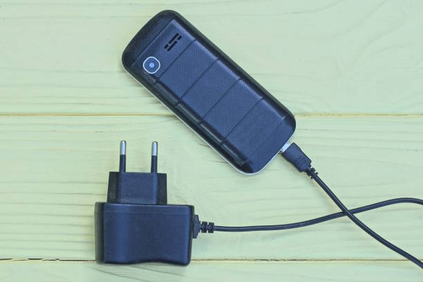 one old black mobile phone and charger lie on a yellow wooden table