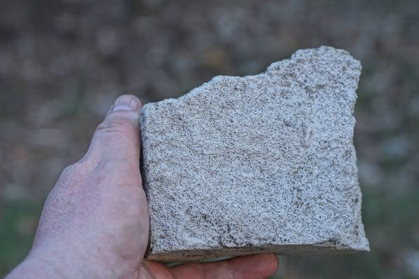a man hand holds a large gray white piece of stone on a summer street