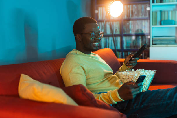istock Young man using phone and watching TV at home 2148443058