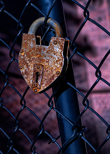 Heart-shaped rusty padlock on a black, chain-link fence.