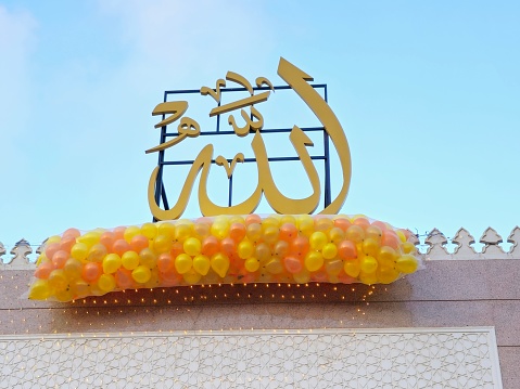 Translation of Arabic text (Allah, The God), festive and celebrations outside a mosque in Cairo with tens of balloons held in the mosque's roof beside the minaret to be thrown for kids for Feast, selective focus