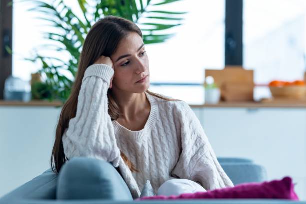 Depressed young woman thinking about her problems while sitting on the sofa at home. Shot of depressed young woman thinking about her problems while sitting on the sofa at home. worried stock pictures, royalty-free photos & images