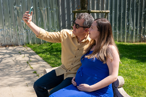 Man and pregnant woman take a selfie in park
