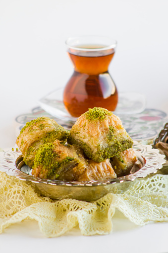 Traditional Turkish pastry dessert dry Baklava designed on white surface with vintage bowl,handmade lace cloth and tea.