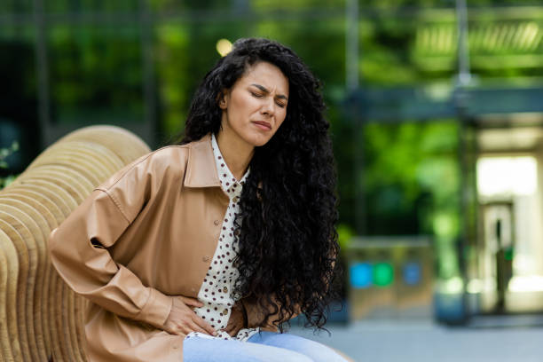 istock Elegant caucasian lady feeling abdominal ache while having break in outdoors resting area. Upset female with curly hair touching stomach and expressing painful emotions. Urban park 2148445584