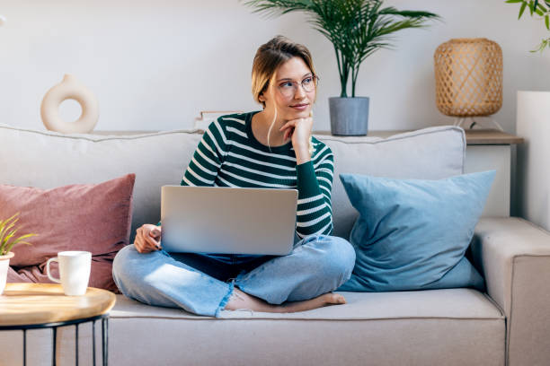 istock Pretty young woman working with her laptop while sitting on couch at home. 2148445669