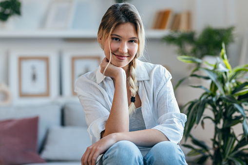 Portrait of beautiful woman looking at camera while sitting on couch in living room at home