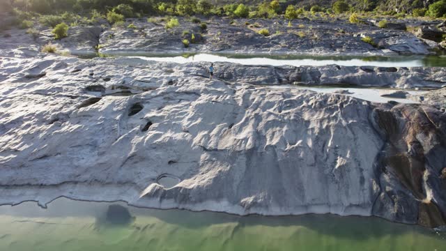 drone tracking person walking over rocks and water at state park during sunset