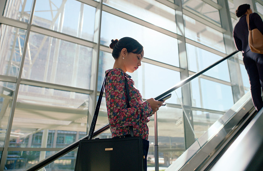 Phone, escalator and business woman at airport for company travel, seminar or meeting in city. Technology, networking and professional female person on cellphone for reading email in stairs in town.