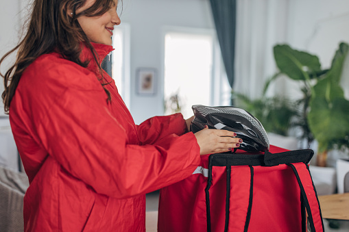 Smiling young caucasian woman in a cozy interior setting packs a vibrant red jacket into her travel bag