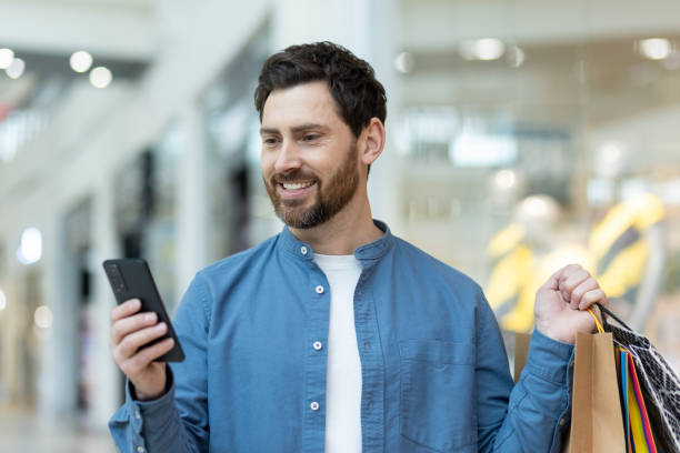 istock Man with shopping bags using smartphone in mall 2148451731