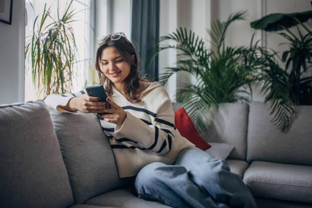 istock Young woman relaxing with smartphone on couch 2148452079