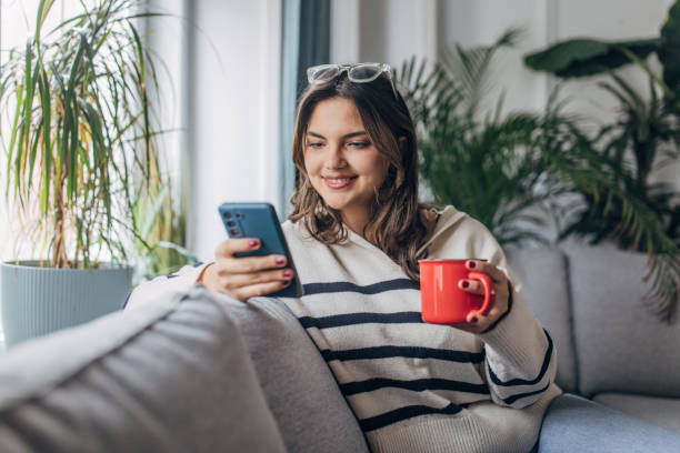 istock Young woman relaxing with smartphone and coffee at home 2148452145