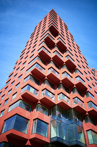 Part of a new multi-story red office building under construction from below, blue sky.