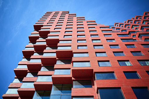 Part of a new multi-story red office building under construction from below, blue sky.