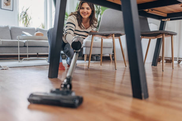 istock Smiling young woman vacuuming under table at home 2148452818