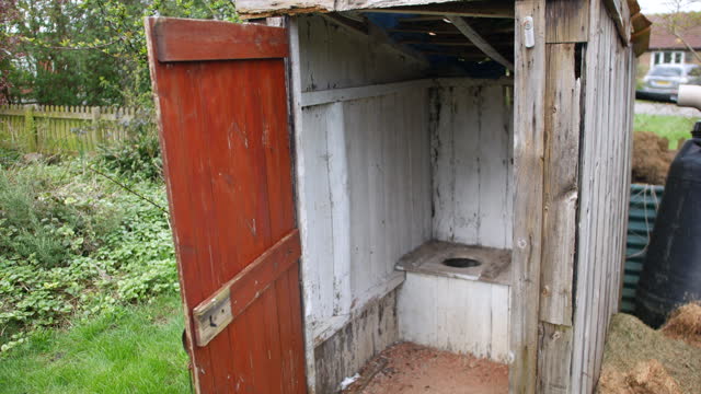 Old wooden outhouse toilet with open door, displaying rustic toilet, set in a green rural setting. Vintage sanitation facility, suitable for historical or rustic themes