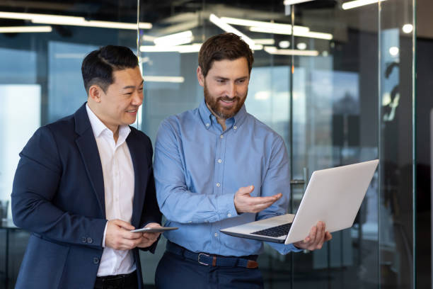 Professional businessmen discussing strategy with laptop in modern office setting Two professional businessmen collaborate using a laptop in a contemporary office environment, demonstrating teamwork and partnership. office buddies stock pictures, royalty-free photos & images