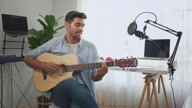 Caucasian man play guitar and produce electronic soundtrack at home. Attractive male artist musician composing, create new song using musical instrument and audio equipment in recording music studio.