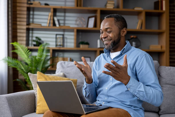 istock Man sitting on sofa at home, joyful african american man smiling using laptop for video call, talking with friends and colleagues remotely 2148459354