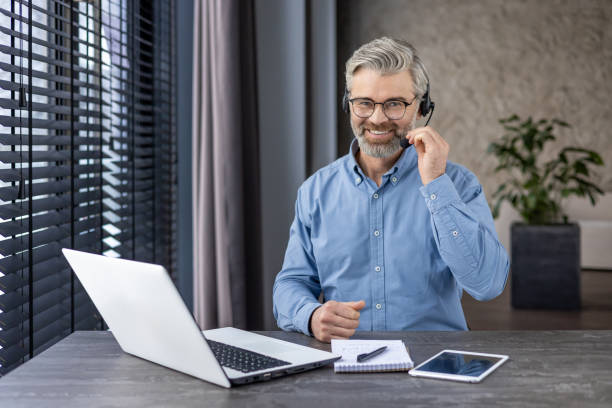 istock Portrait of mature successful gray haired man inside office at workplace inside office, businessman with headset phone and laptop for video call smiling and looking at camera 2148460035