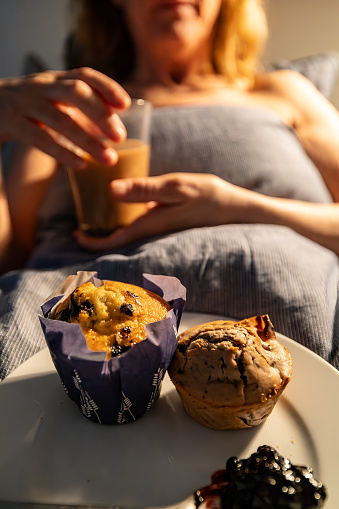 A woman is served coffee, muffins and jam in bed.
