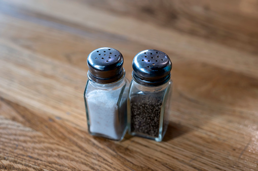 Salt shaker spilling salt. Salt is a spice used for seasoning for preserving food. The image is shown at an angle, and is in full focus from front to back. The image is isolated on a white background, and includes a clipping path.