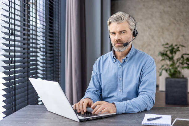 istock Professional middle-aged man with headset working on laptop in modern office setting, focused customer service 2148462598