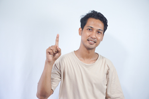 Attractive young man in cream t-shirt pointing up with his finger isolated on gray background
