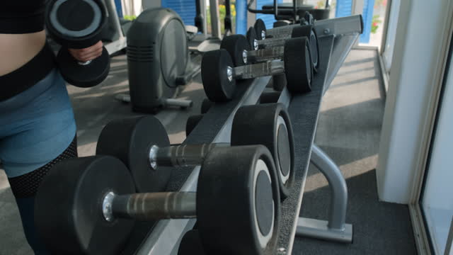 Close-up of woman taking dumbbells from the rack