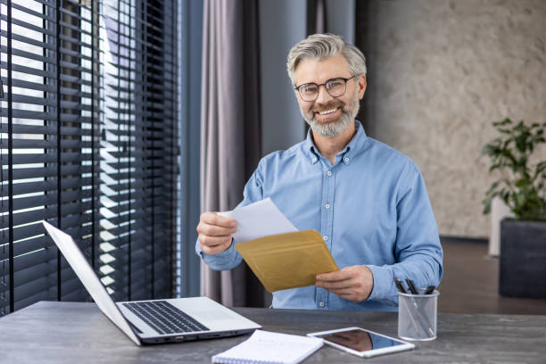 istock Confident mature businessman with glasses smiling while holding documents in a modern office setting 2148463990