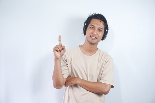 Asian man wearing headphones smiling amazed and surprised and pointing up with fingers and raised arms. isolated on white background