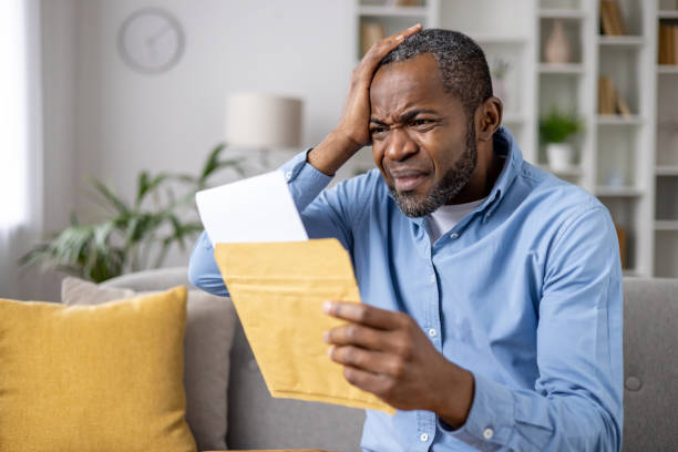 istock Senior gray haired man upset received envelope mail message notification with bad news, sad displeased and disagreeable african american man sitting at home on sofa inside living room 2148465325