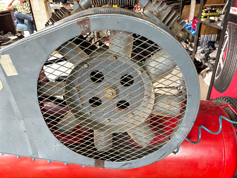 A red and grey machine, air compressor with a fan on it. The fan is covered in a mesh