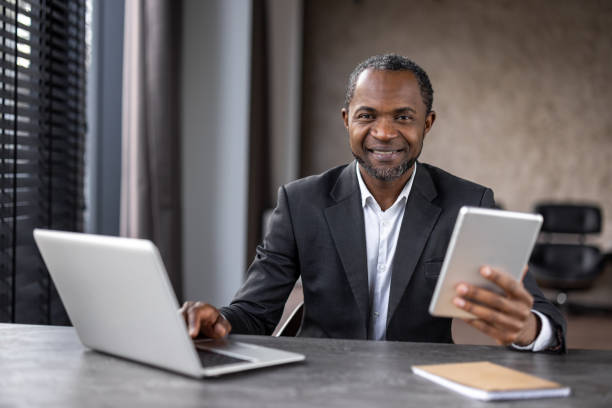 istock A man in a suit is sitting at a desk with two laptops and a tablet 2148466538