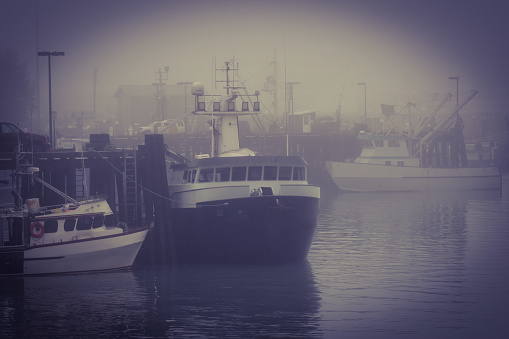 Tapia de Casariego harbor in thick fog, touristic location. Rows of moored fishing boats defocused, stone dock, lighthouse .