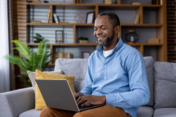 istock Smiling african american man using laptop at home on comfortable sofa 2148468395