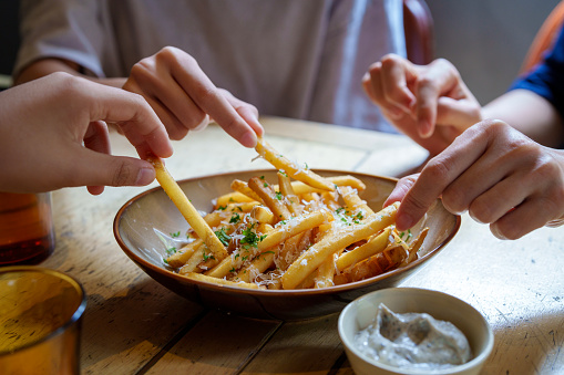 Friends sharing and enjoying fries topped with Parmesan cheese and truffled mayonnaise sauce.