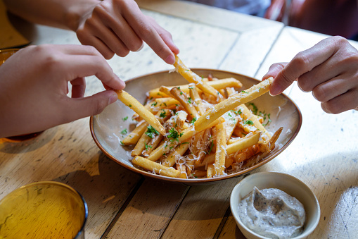 Friends sharing and enjoying fries topped with Parmesan cheese and truffled mayonnaise sauce.