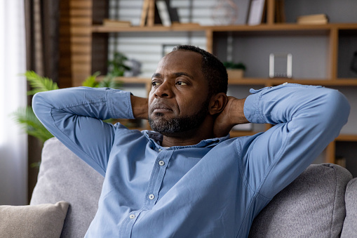 Portrait of a thoughtful African American man lounging on a couch, looking reflective and calm in a comfortable indoor setting.
