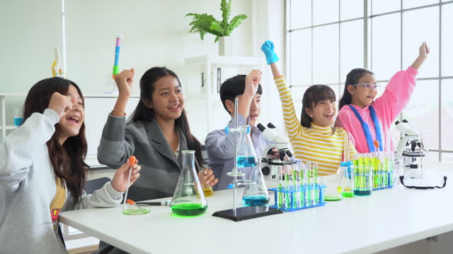 group of excited asian school kid doing chemical experiment in laboratory raise hand up together. happy pupil students science testing chemistry class in the lab at school