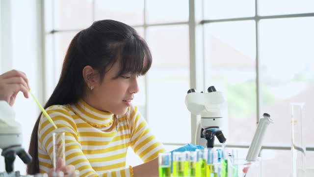 asian schoolgirl pupil student looking through microscope during science practical class in school laboratory. asia children scientists learning  biology chemistry lesson . Elementary School Science
